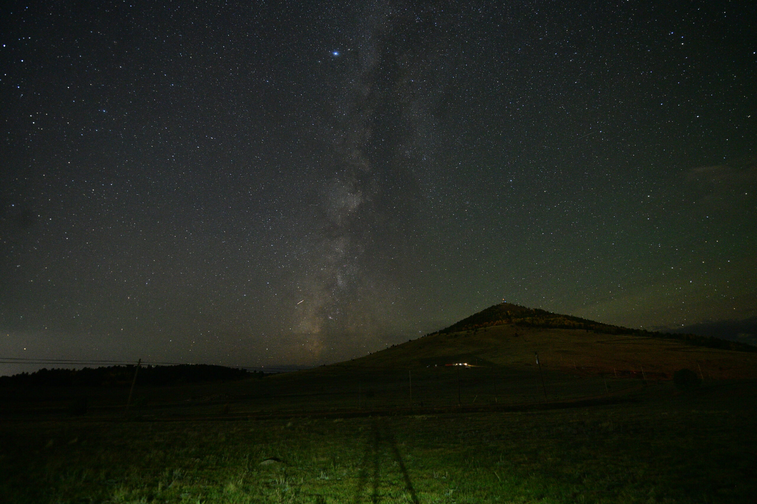 Camera preview of the Milky Way above a dark hillside, with power lines and poles in the foreground.